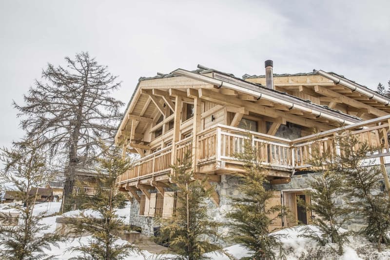 large wooden chalet, stone base, wooden terrace, chimney, multiple windows, wooden shutters