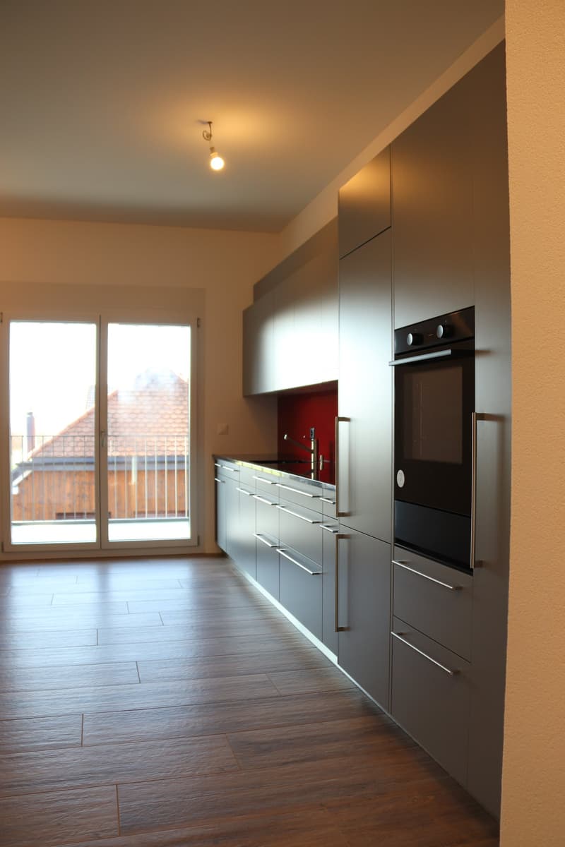 modern kitchen with wooden floors, gray cabinets, black oven, sliding door leading to balcony