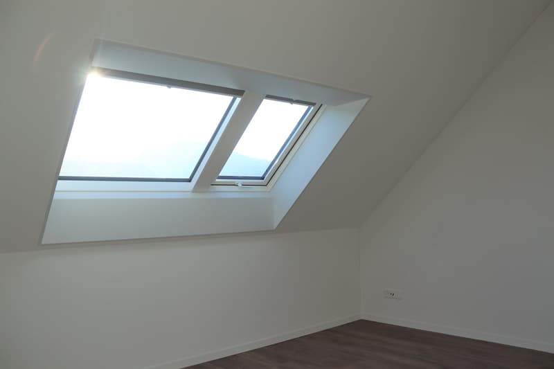 empty attic room with two dormer windows, white walls, wooden floor