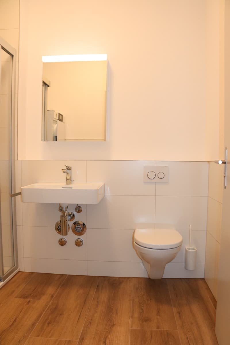 tiled walls, white fixtures, wooden floor, shower enclosure
