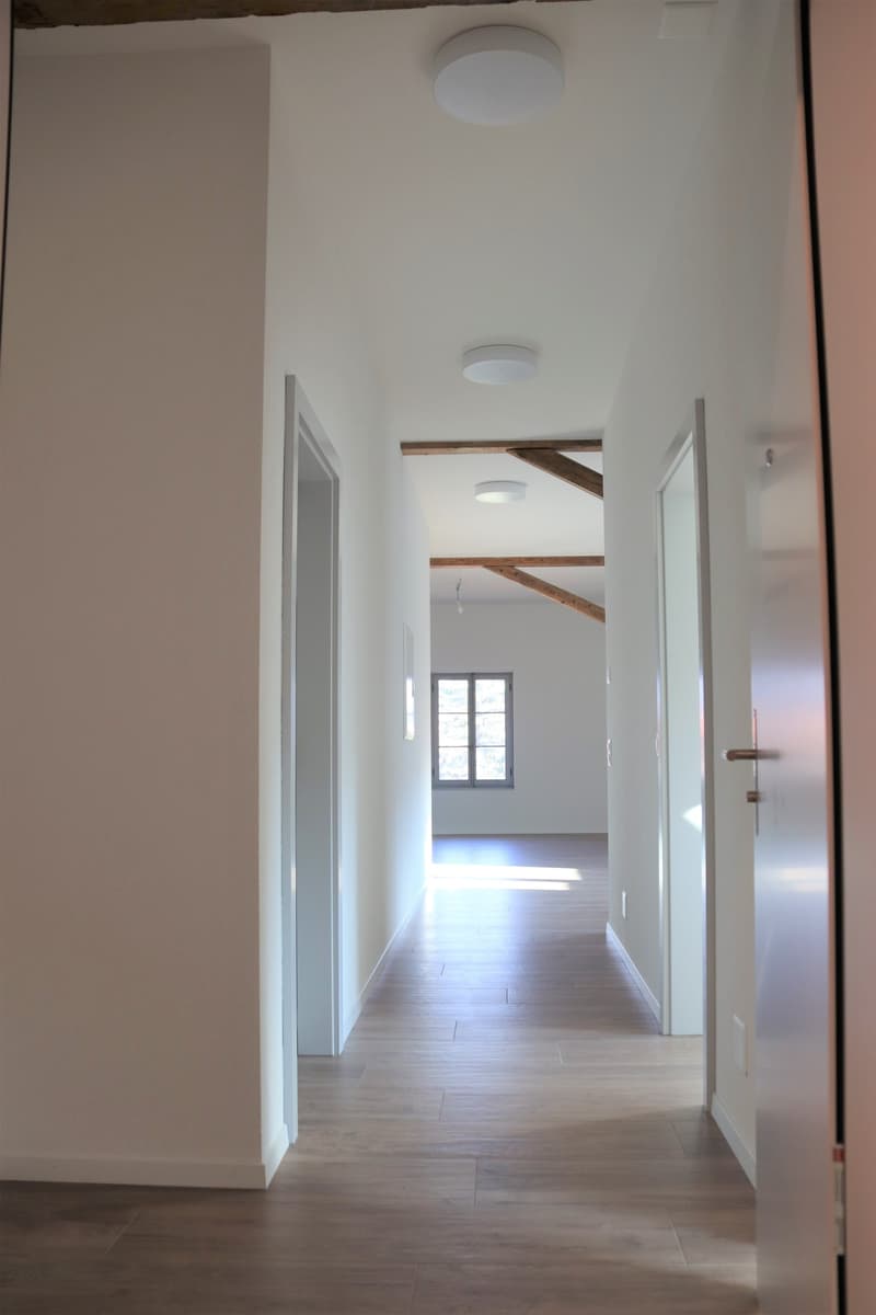 corridor with wooden floor, three ceiling lights, white walls, two room doors, a small window