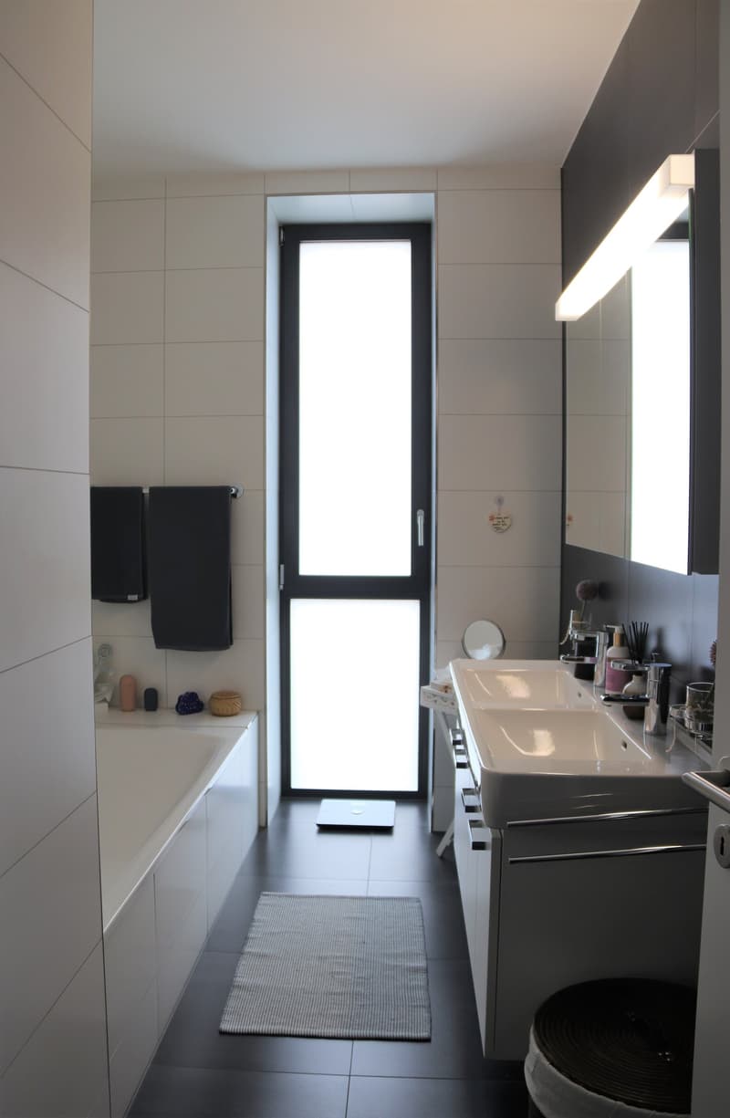 modern bathroom, white tiles, bathtub, double sink, mirror, towel rack, floor mat