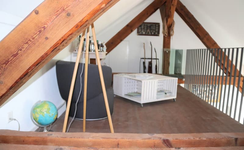 attic room with wooden beams, wooden floor, black chair, white coffee table, globe, guitars