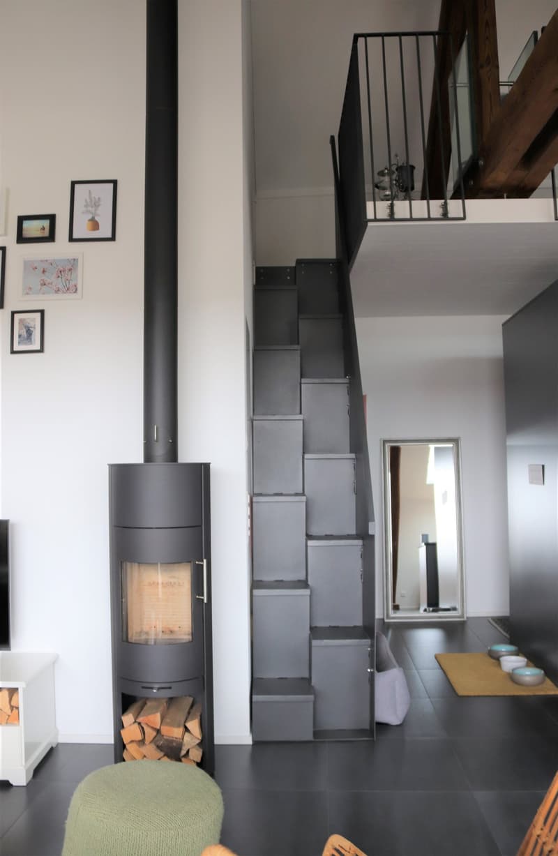 Fireplace, black stove, wooden stairs, white walls, black floor, mirror, picture frames