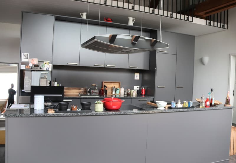 modern kitchen, gray cabinets, granite countertop, stainless steel range hood, red pot, black bowls, bottles, and other kitchen items