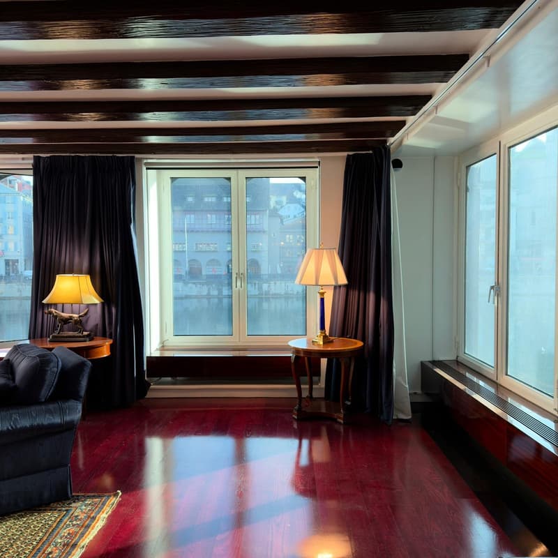 Living room with red wooden floor, large windows, two lamps, couch, rug, black curtains