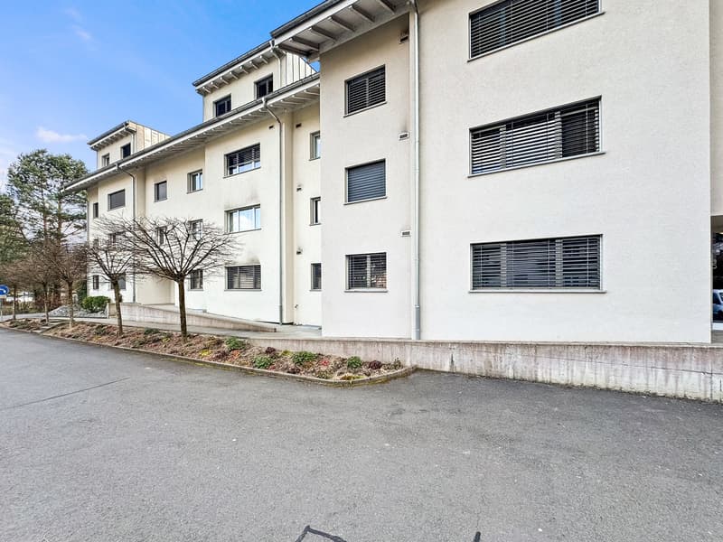4 story apartment building, white exterior, multiple windows, parking area in front, possible garage