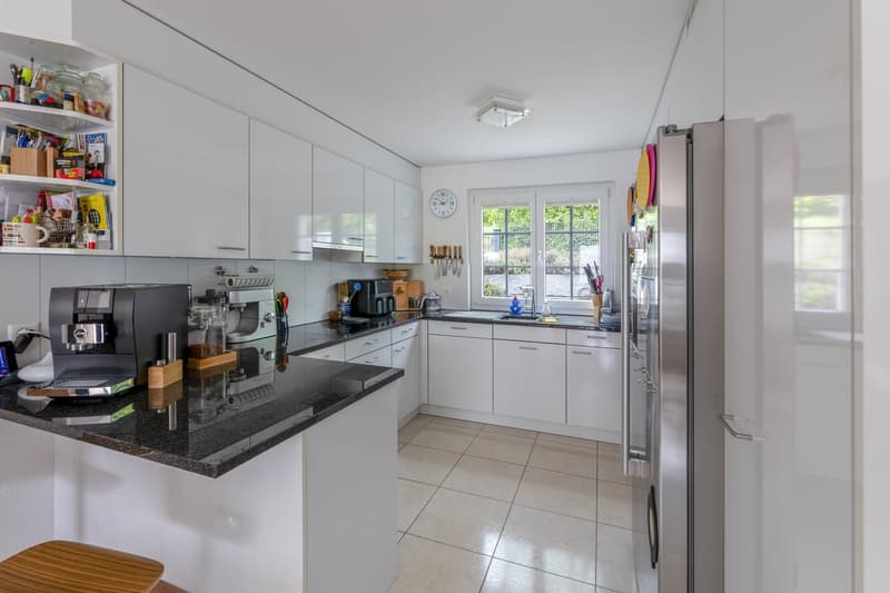 modern kitchen with white cabinets, black granite countertop, stainless steel appliances, wooden stool, open door to the garden