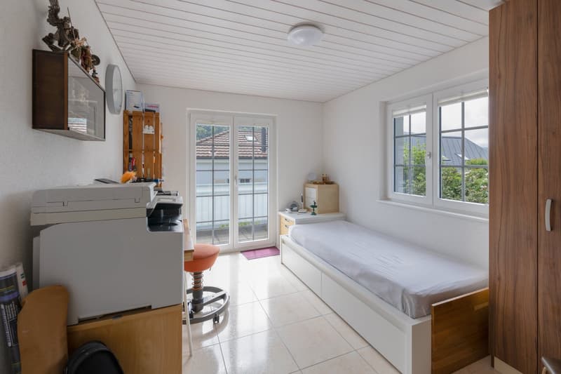 small room with bed, printer, stool, shelves, windows, and a door