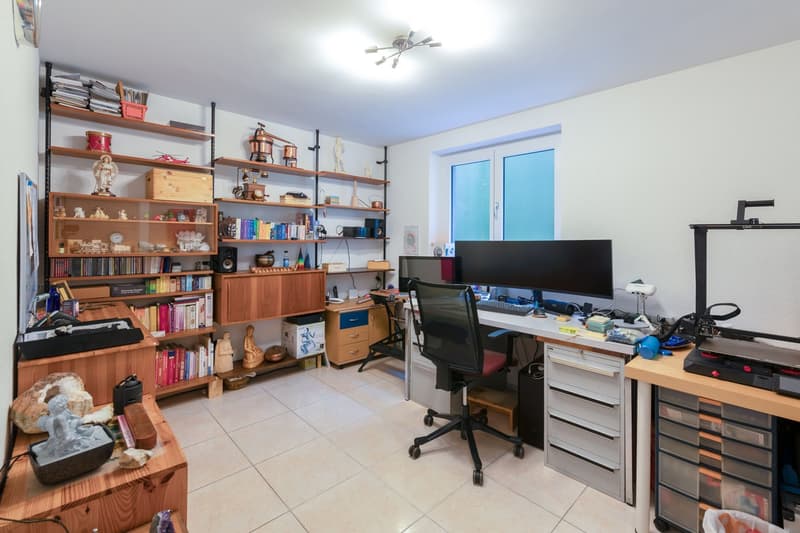 A room with a desk, chair, shelves, and various items on display.