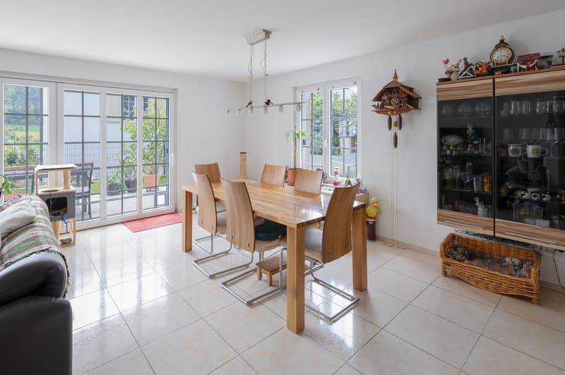 Dining room with wooden table, chairs, sliding glass doors, tiled floor, and a cabinet with glass doors
