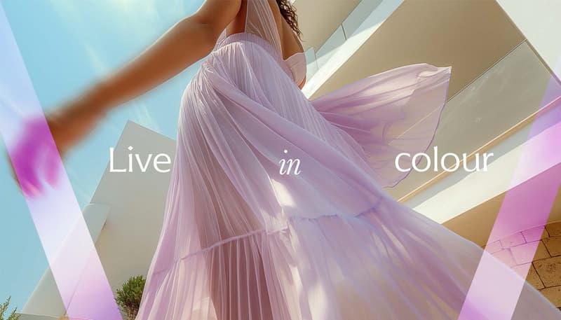The image shows a close-up view of a flowing, pleated lavender dress or gown. The dress has a halter-style neckline and the fabric appears to be lightweight and sheer, creating a dramatic, billowing effect. The text overlay on the image reads 'Live in col