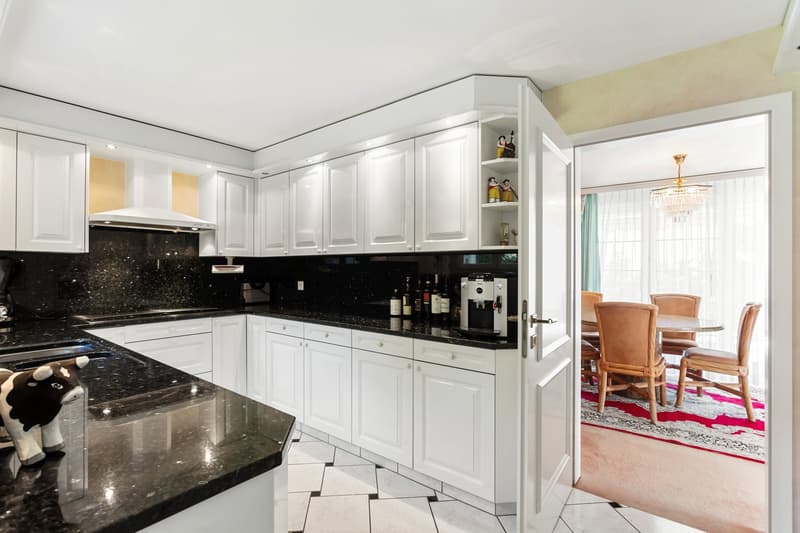 modern kitchen with white cabinets, black granite countertops, marble flooring, open to dining area with round table and chairs, chandelier, rug