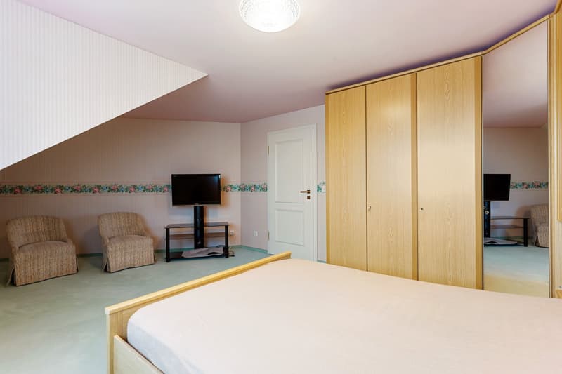 Bedroom with bed, two armchairs, TV, wardrobe, and a ceiling lamp