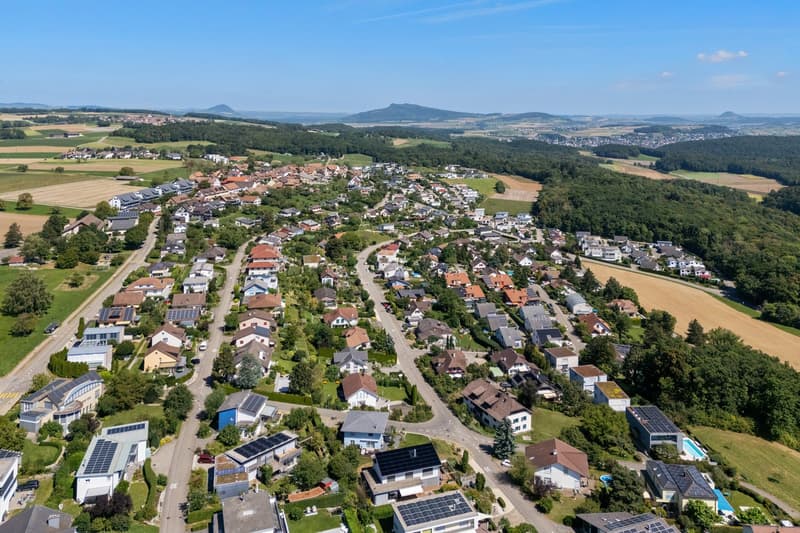 Aerial view of a residential area with many houses, solar panels, and green surroundings.