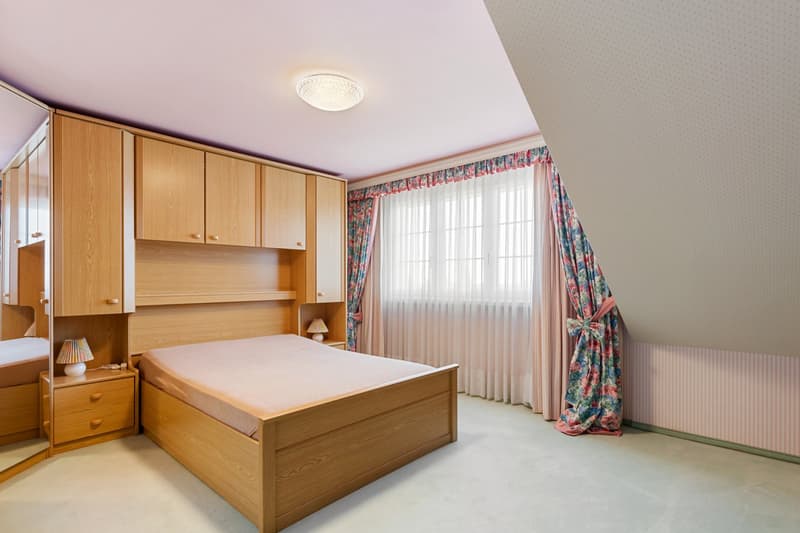Bedroom with wooden bed, wooden cabinets, lamps, mirror, and floral curtains