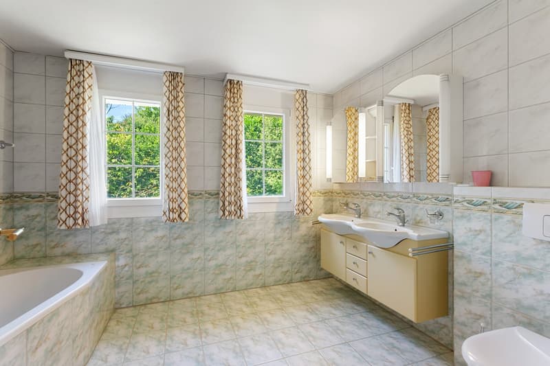 Bathroom with bathtub, double sink, mirror, and toilet.