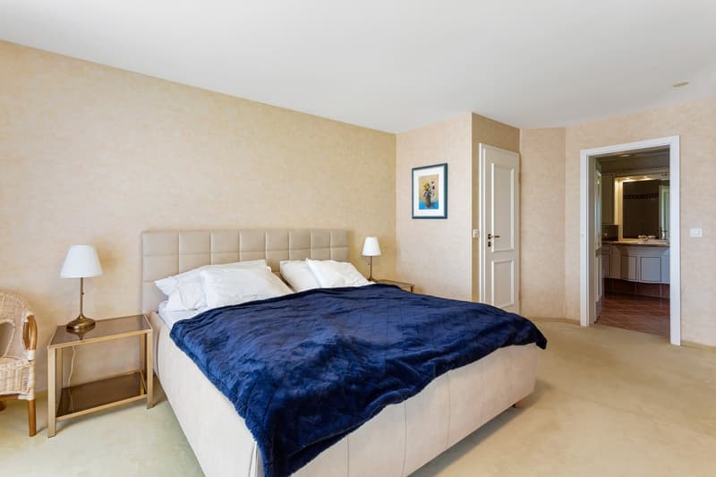 A bedroom with a bed, nightstands, lamps, and a picture frame on the wall. The room has a door leading to a bathroom.