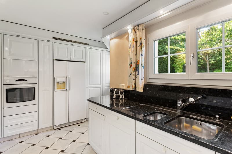 modern kitchen with white cabinets, black granite countertops, stainless steel sink, refrigerator, oven, dishwasher, and a window with a view of trees