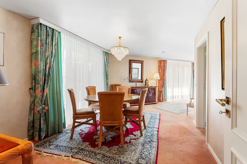 Dining room with round table, wooden chairs, chandelier, carpet, sideboard, mirror, lamps, curtains, picture frame