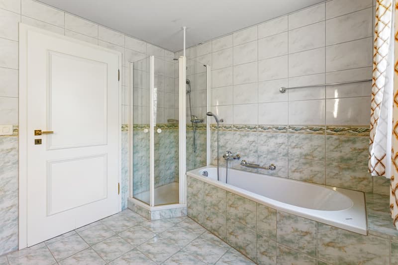 Bathroom with white tiles, bathtub, shower, and a white door.