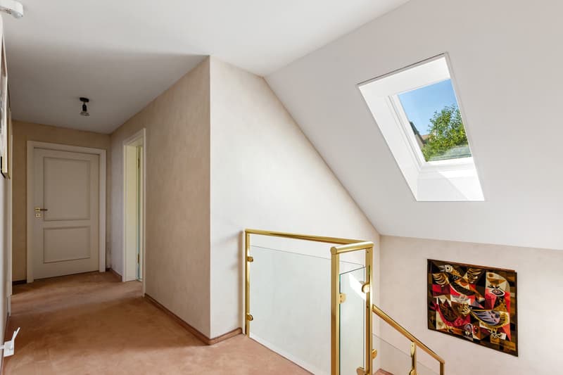 staircase with gold railing, white walls, beige flooring, skylight, artwork