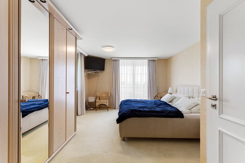 large bedroom with bed, TV, chair, nightstand, large closet, mirror