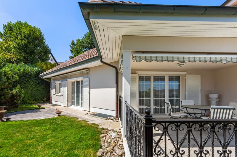 white exterior, brown roof, large windows, balcony with table and chairs, garden with green grass