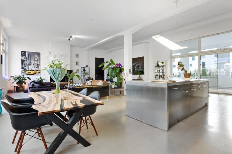 modern open plan living room with dining area, large windows, stainless steel kitchen island, wooden dining table, black chairs, plants, artwork