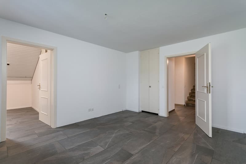 Empty room with white walls, gray tile flooring, and multiple doorways leading to other rooms.