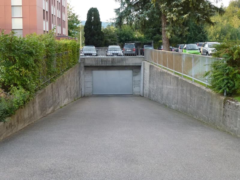 Asphalt parking lot with multiple parked cars, leading to a garage door.