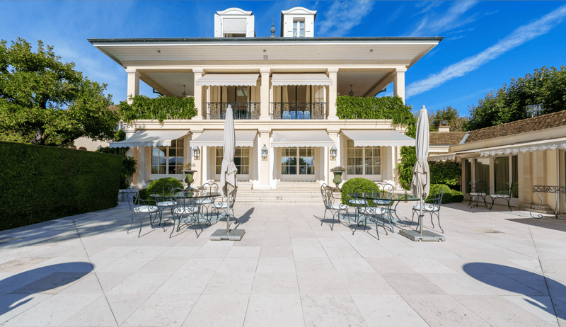 large house with white marble facade, white windows, terrace with tables, plants