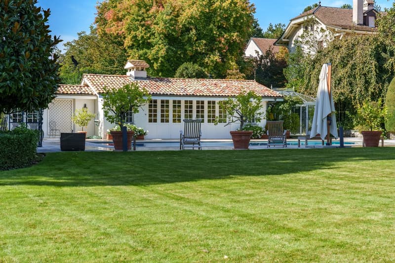 well-maintained garden with neatly trimmed lawn, decorative potted plants, pool, and chairs
