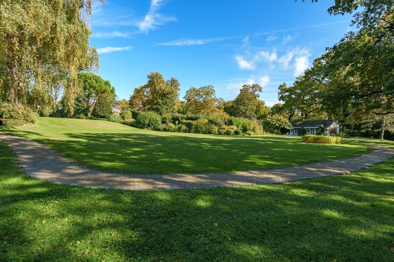Large, well-maintained lawn with a central pathway, surrounded by trees and bushes.