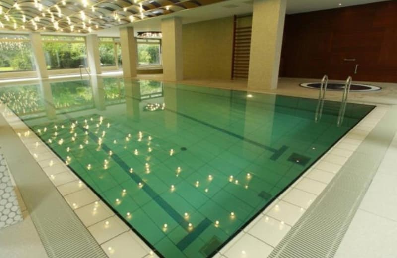Large indoor swimming pool, clean water, decorative lights on bottom, visible tiles, two white doors