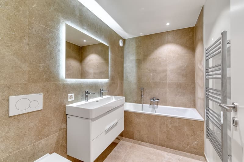 modern bathroom with beige tiles, white bathtub, white sink, mirror, towel rack