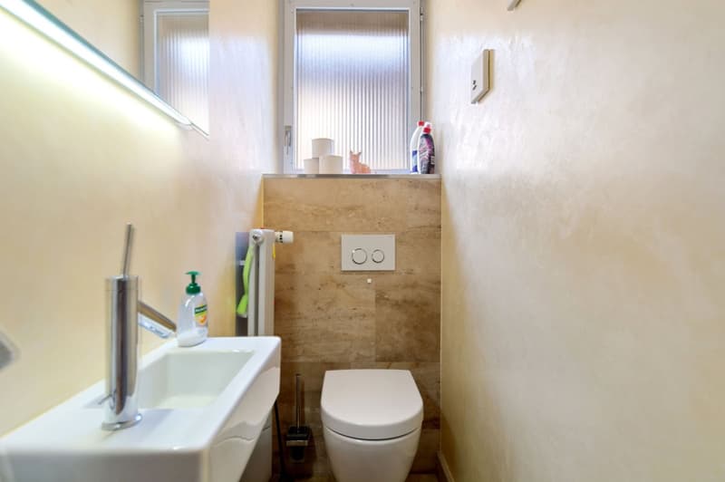 a small bathroom with a sink, toilet, white tiled wall, and white toilet