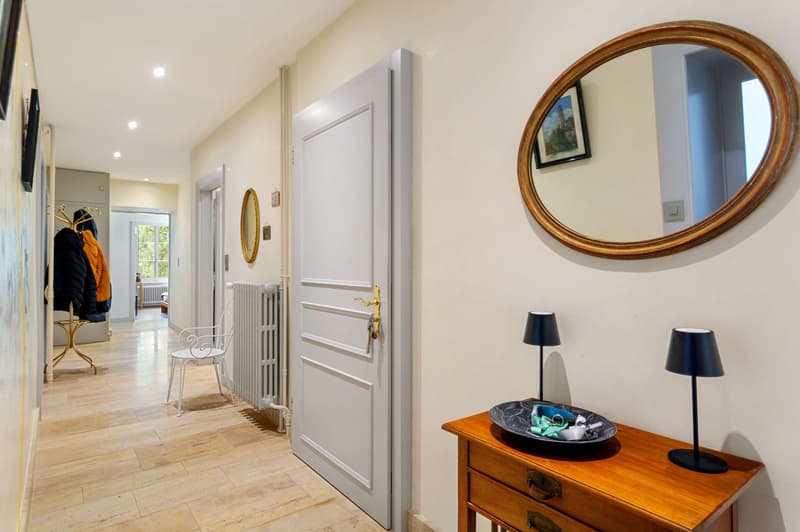 hallway, wooden floor, white door, radiator, table with lamps and bowl, mirror on the wall, framed picture