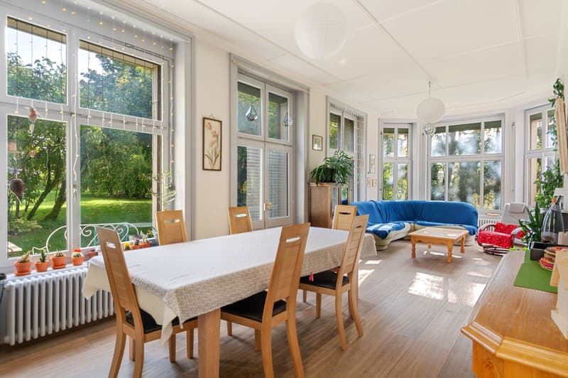 dining room with large windows, view of a green lawn, sofa, coffee table, potted plants