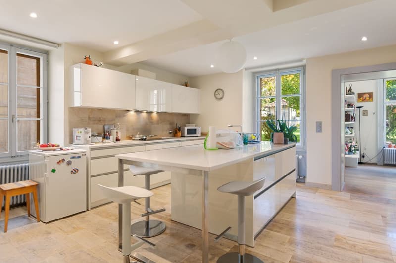 Island kitchen with appliances, modern countertops, white cabinets, stainless steel faucet, chairs at the island, white fridge, white modern flooring