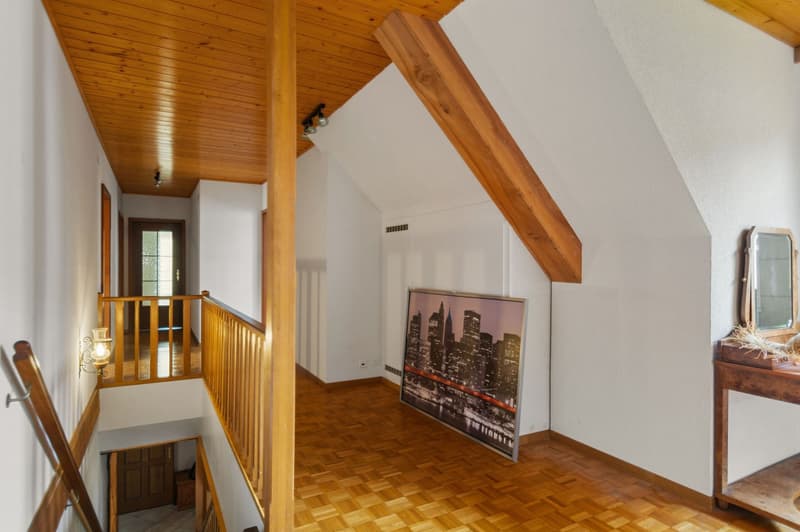 Interior room with wooden floors, ceiling beams, and wooden railing, wall mounted lamp.