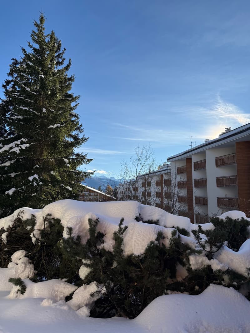 An apartment building with multiple balconies and covered terraces on the exterior facing a snowy landscape.