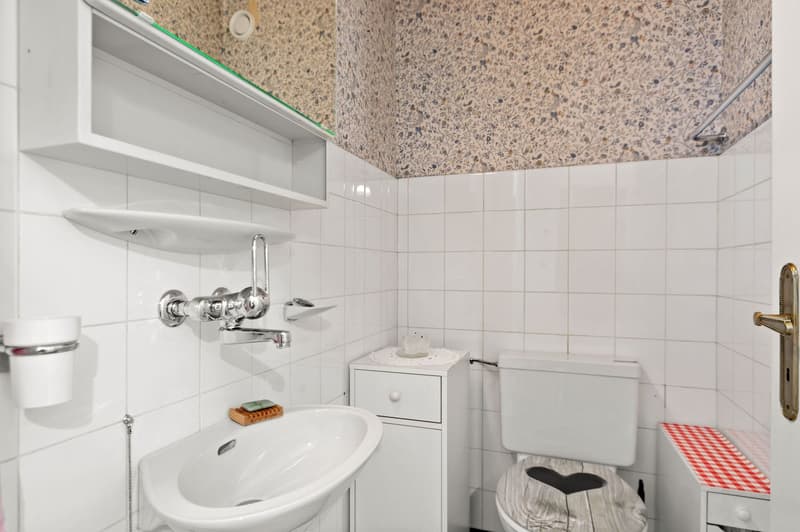 white tile walls, white sink, soap holder, faucet, toilet, red and white checkered toilet cover, white cabinet with drawer, white shelves