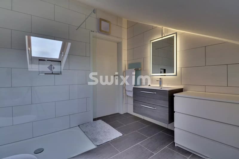 Belle salle de bain moderne avec un éclairage intégré et des surfaces en gris et blanc.