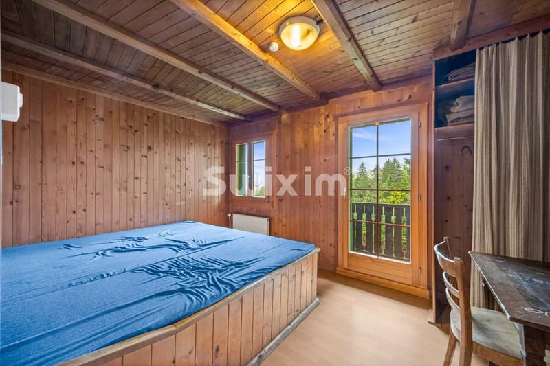 Une chambre chaleureuse en bois avec un lit double, un bureau, et une vue sur la nature à travers une fenêtre.
