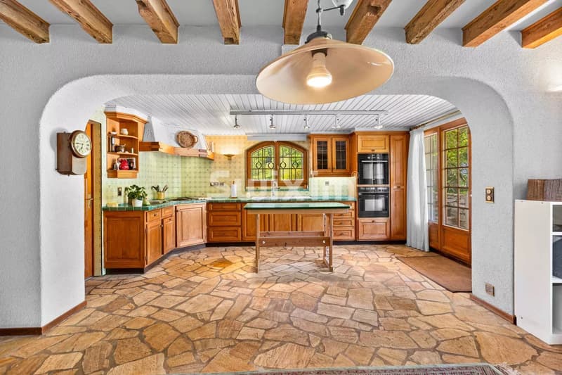 Cuisine rustique avec meubles en bois, plafond à poutres apparentes et sol en pierre.
