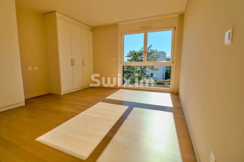 Chambre lumineuse avec parquet et grande fenêtre offrant une belle vue.