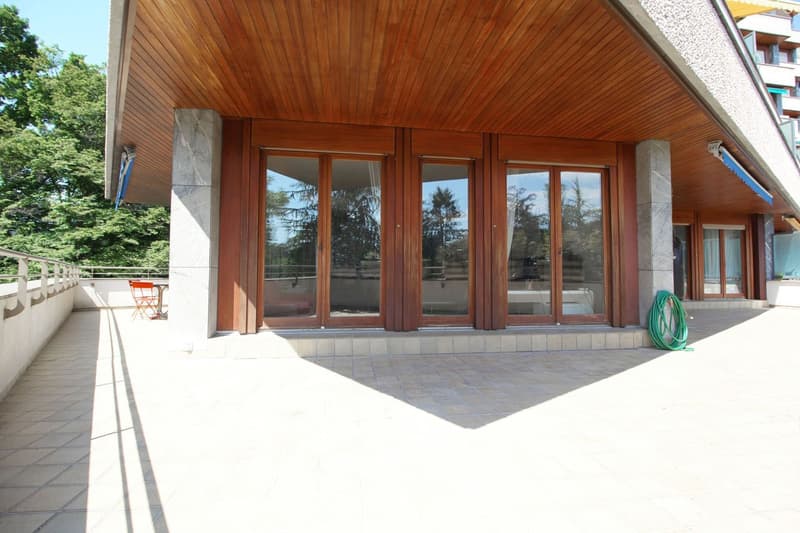 Modern building with wooden facade, glass doors, tiled floor, balcony, and trees in the background
