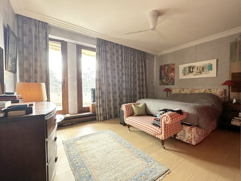 Spacious bedroom, with a bed, wooden floor, two nightstands, a couch, a desk, and an open balcony.