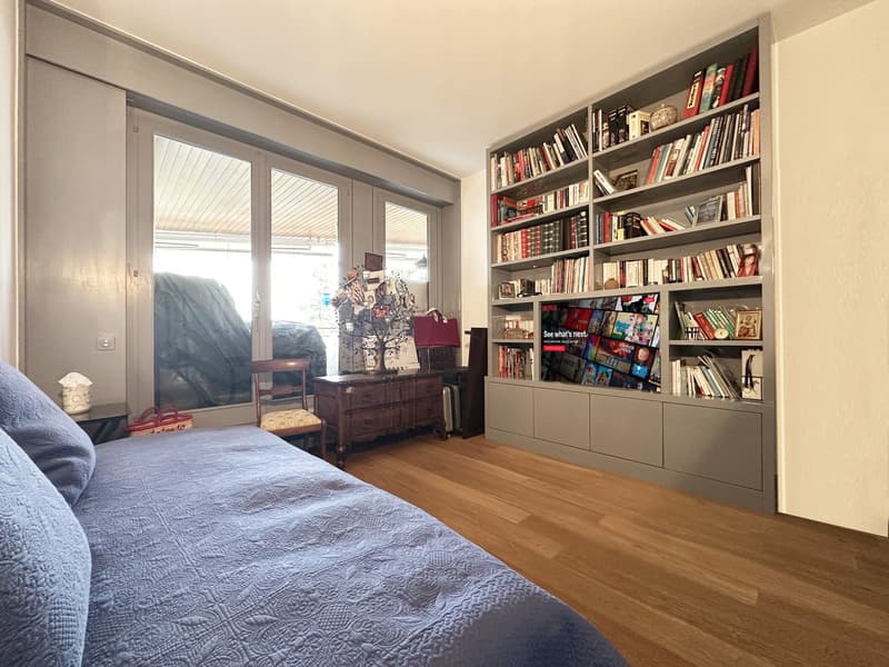 Bedroom with large bed, hardwood floor, large glass door, bookshelf, wooden desk, chair, TV